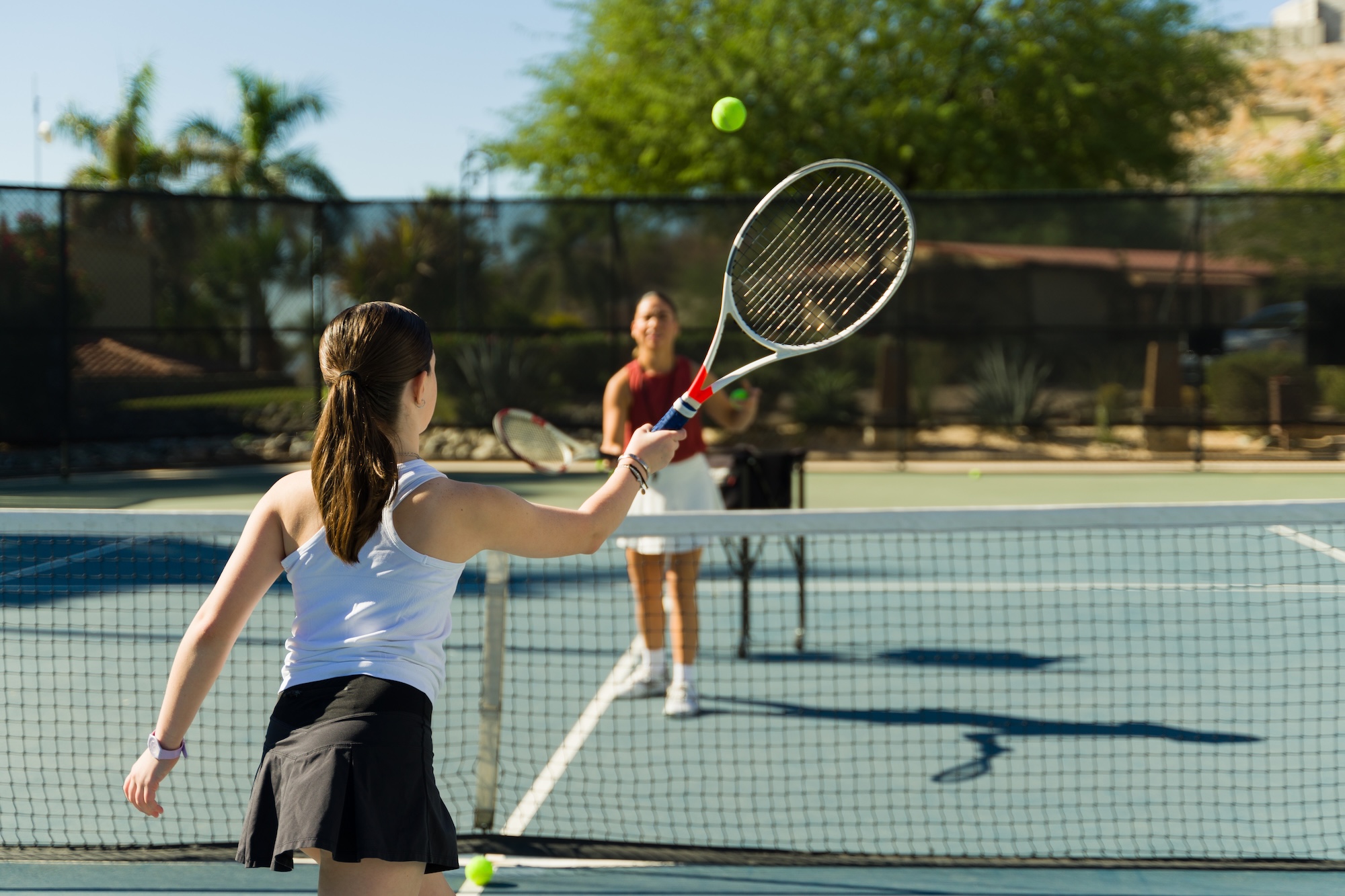 Beautiful teenage girl practicing her forehand using a racket while taking tennis lessons with a coach